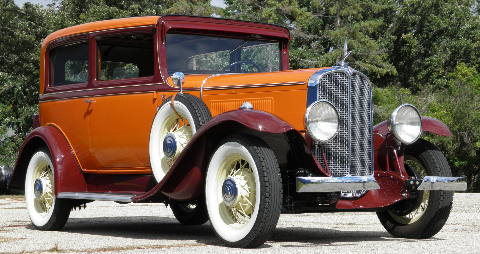 An old orange and red car is parked on a gravel road.