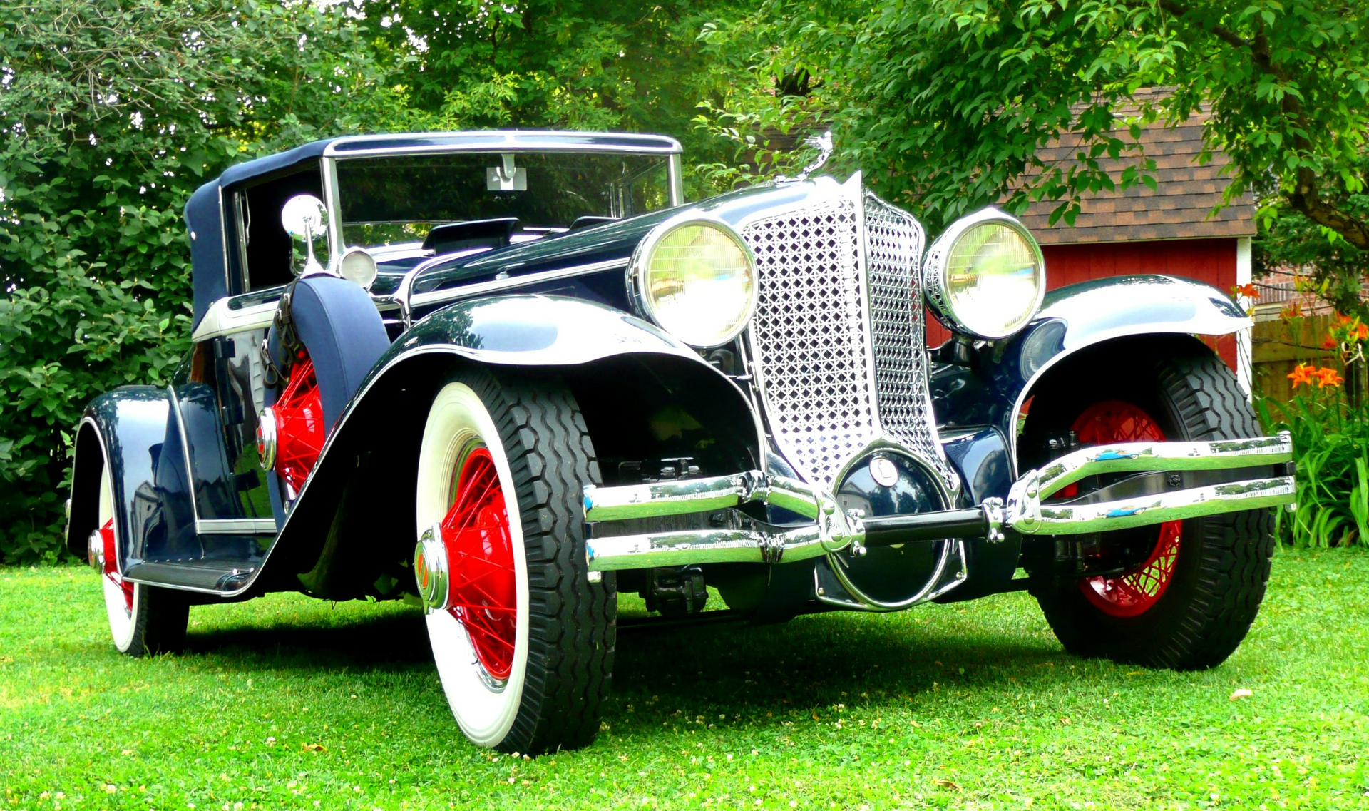 An old car is parked in the grass in front of a red barn