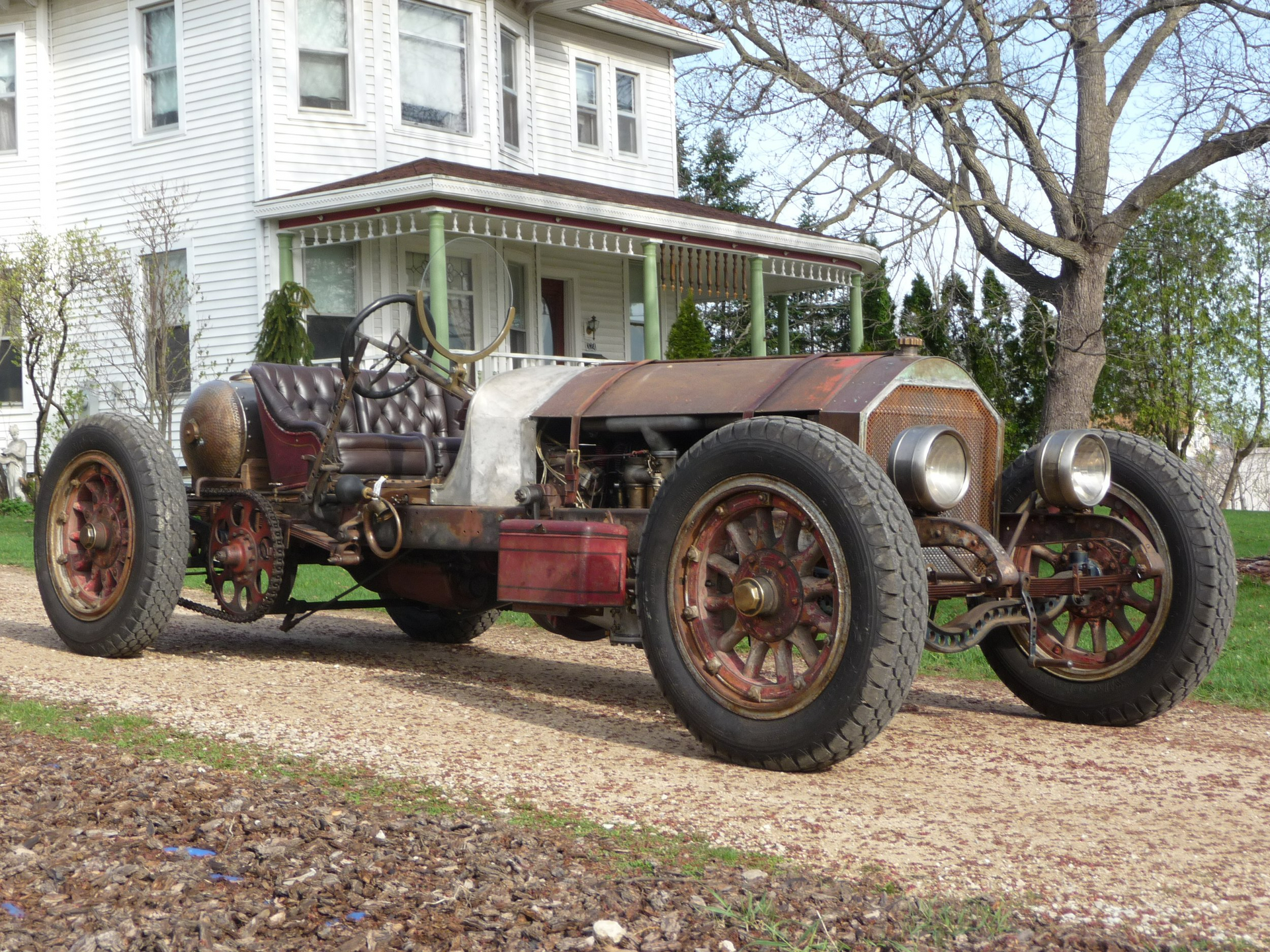 An old rusty car is parked in front of a white house.