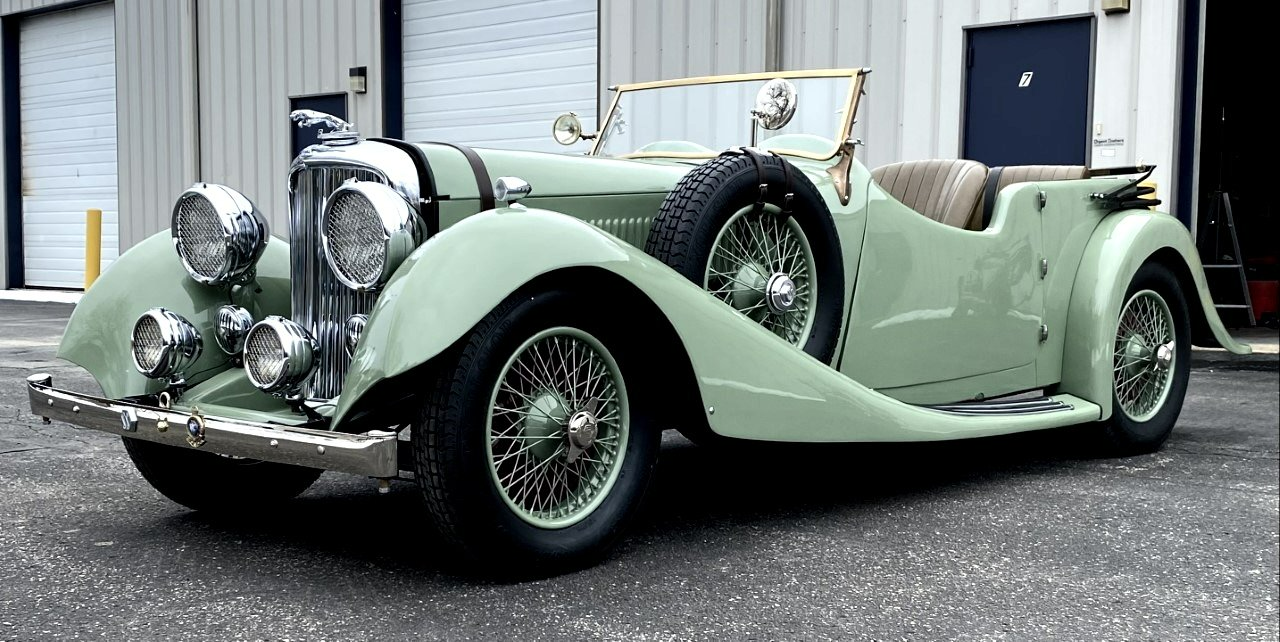 A green vintage car is parked in front of a building.