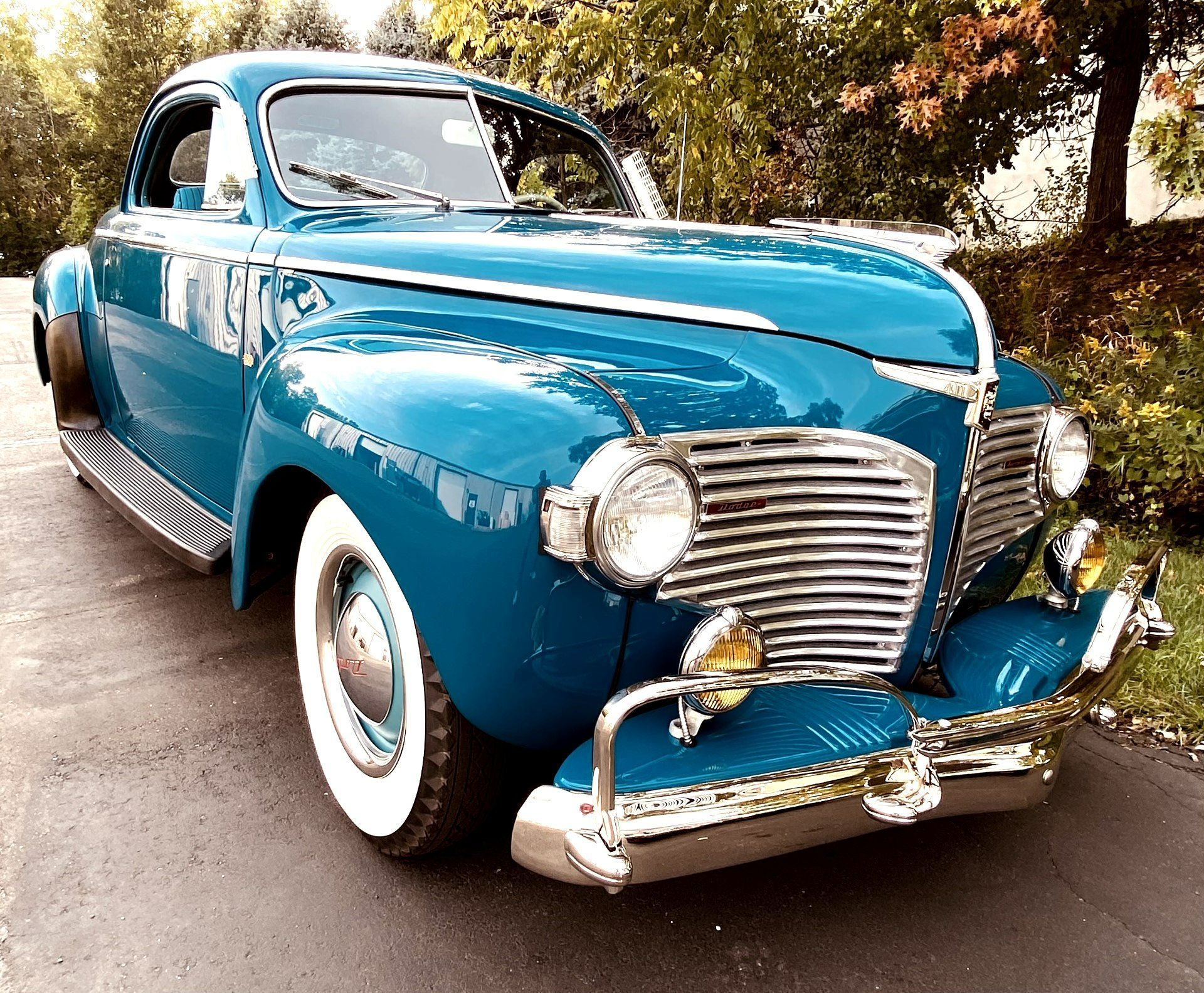 A blue car with white tires is parked on the side of the road