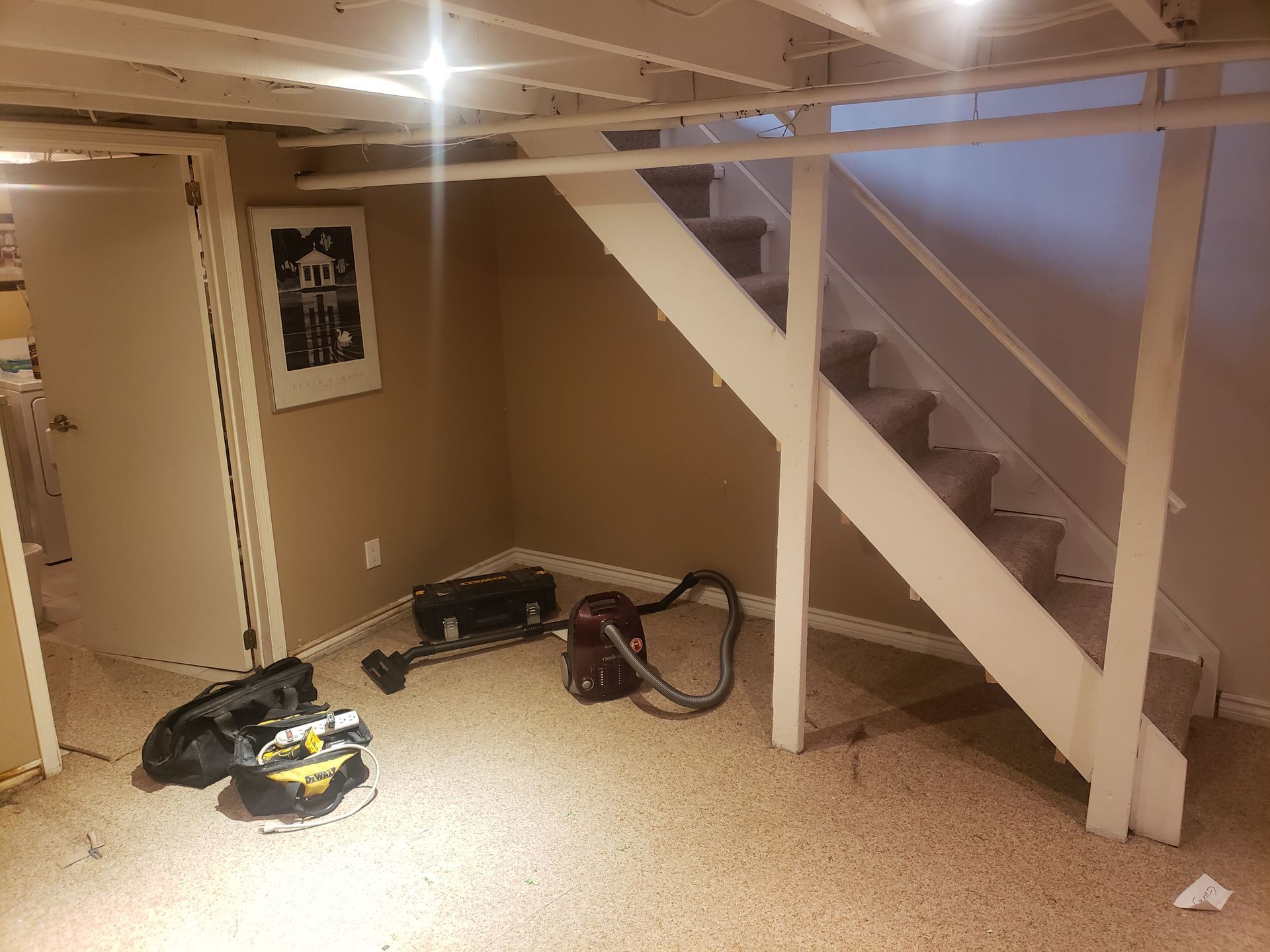 A basement with stairs and a vacuum cleaner on the floor.