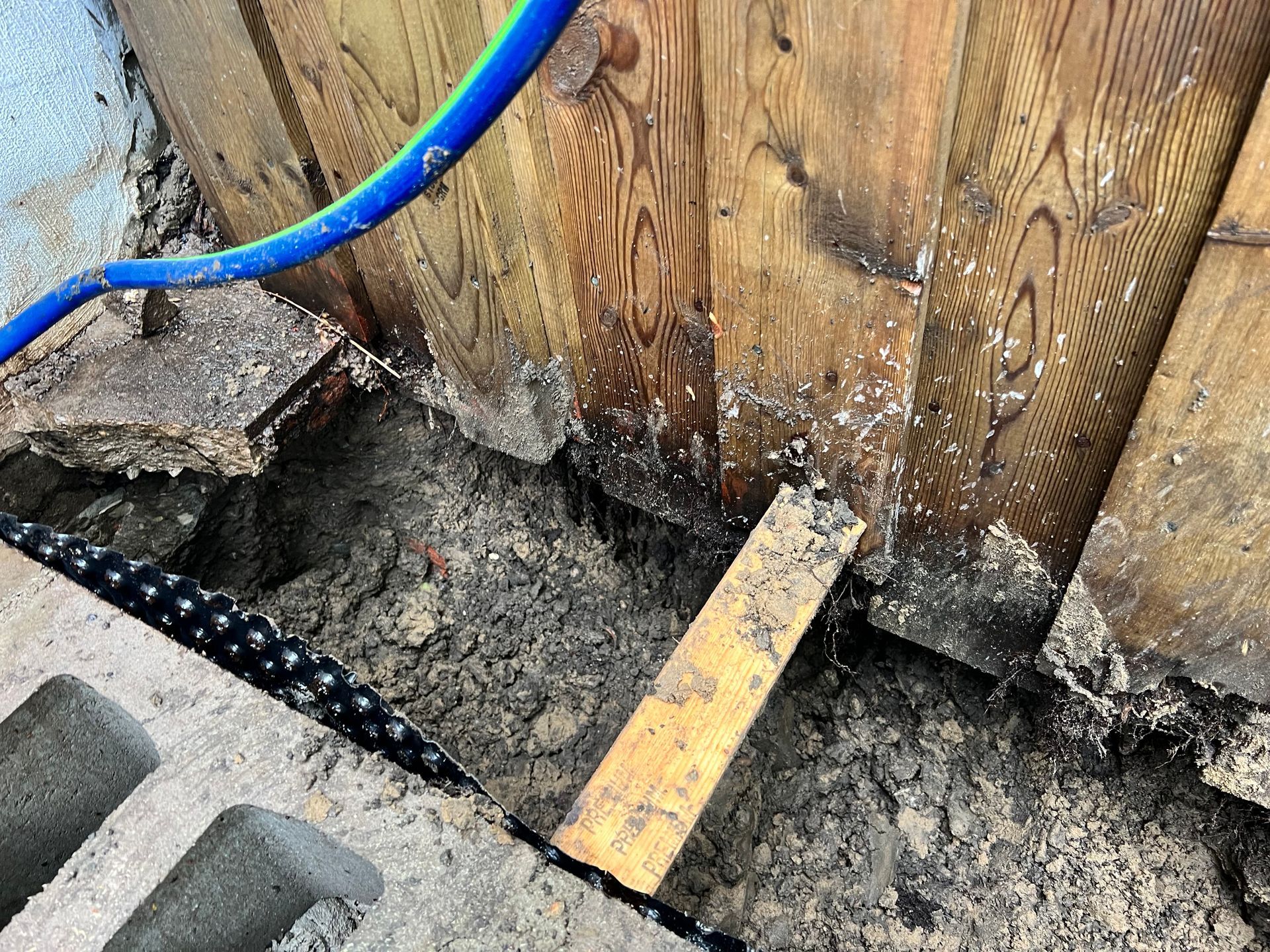 A blue hose is laying on the ground next to a wooden wall.