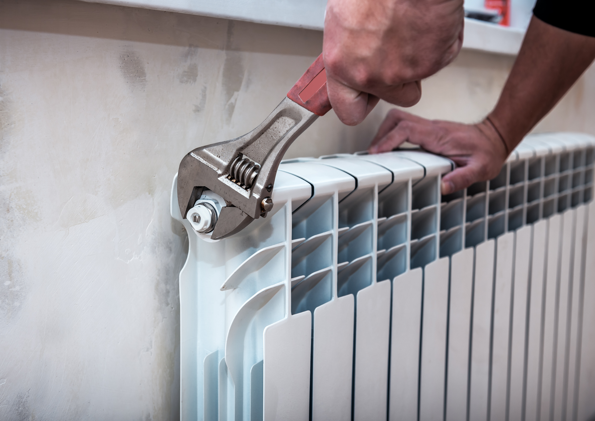 Man adjusting a round, silver smart thermostat on a wall.