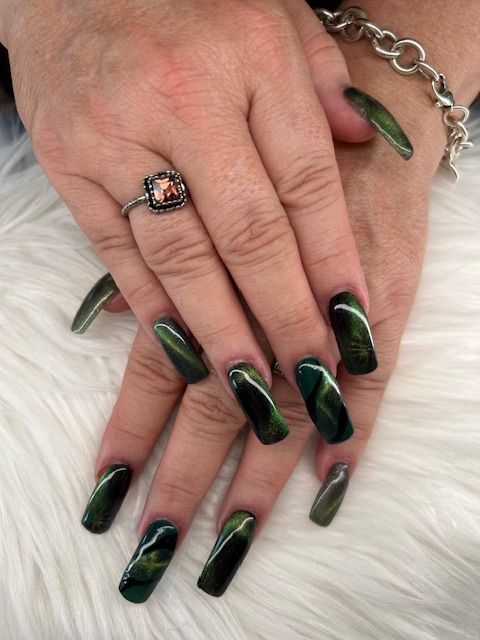 A woman 's hand with long green nails and a ring on her finger.