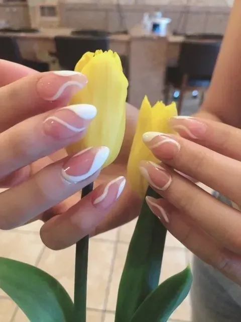 A woman with white nails is holding a yellow flower