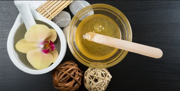 A bowl of wax next to a flower and a spoon.