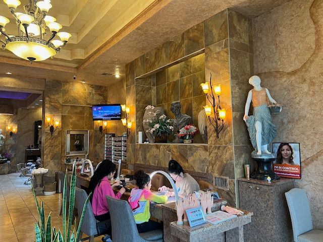 A group of people are sitting at tables in a nail salon.