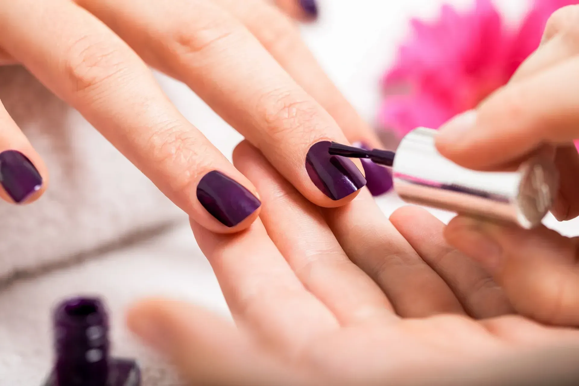 A woman is getting her nails painted with purple nail polish.