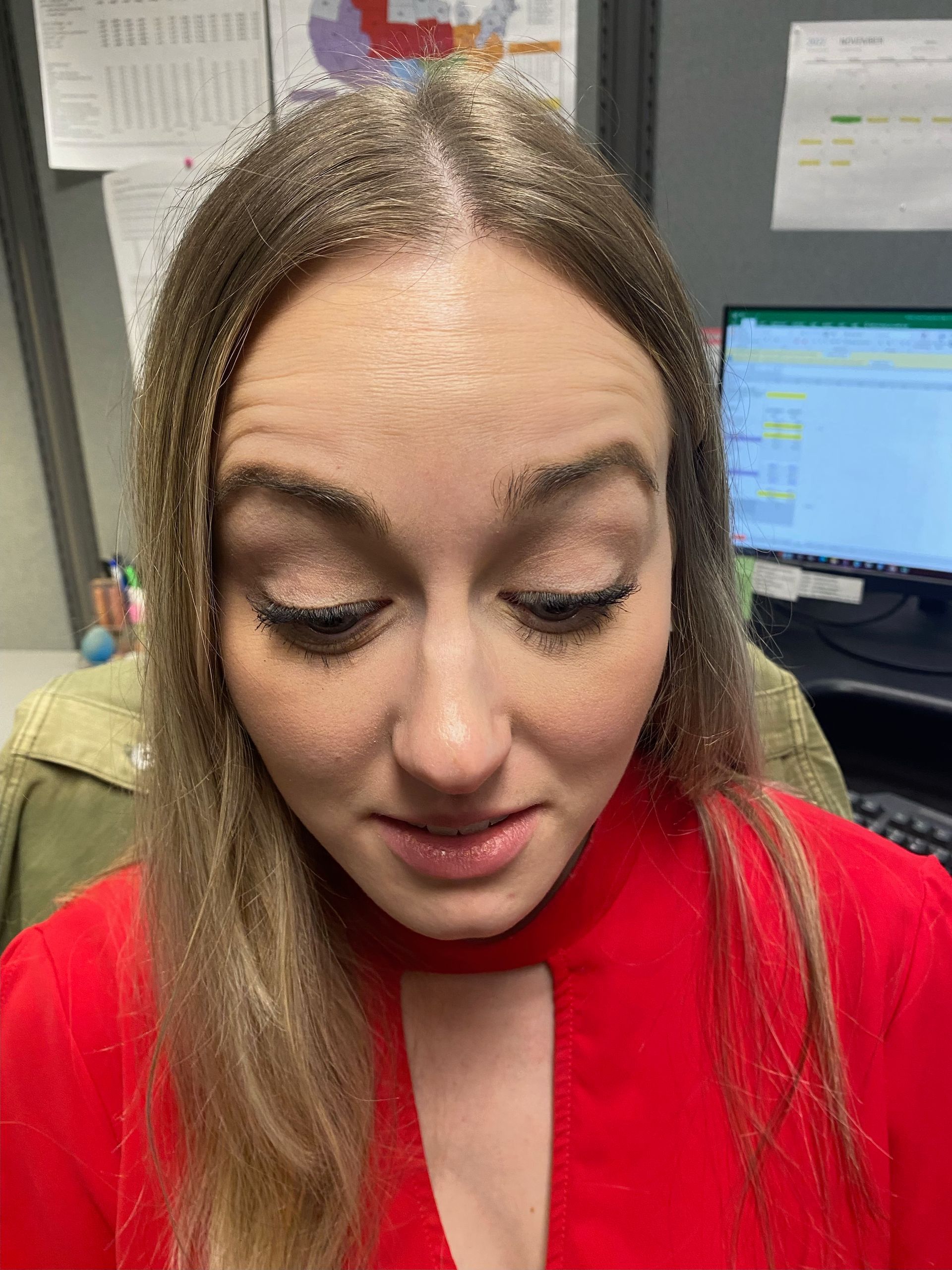 Woman with long blonde hair wearing a red shirt, looking down in an office setting.