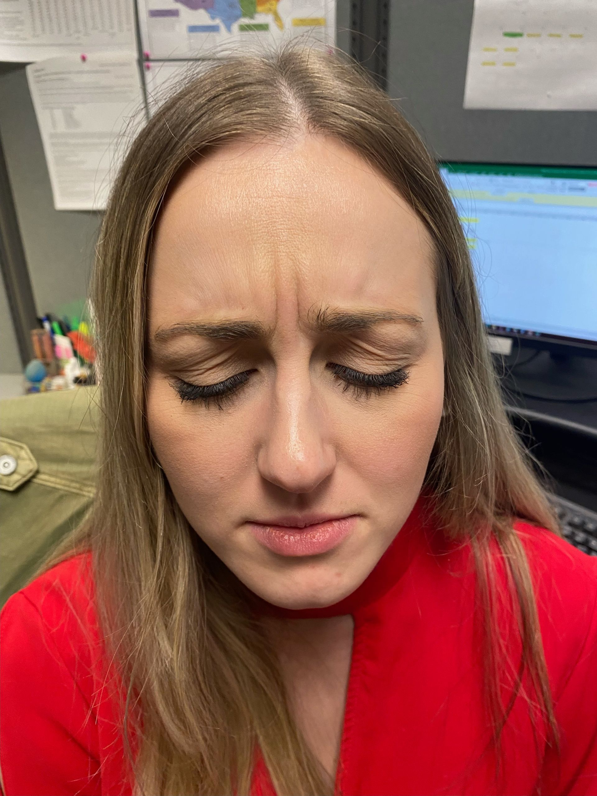 Woman with closed eyes, furrowed brow, and pursed lips, wearing a red top.