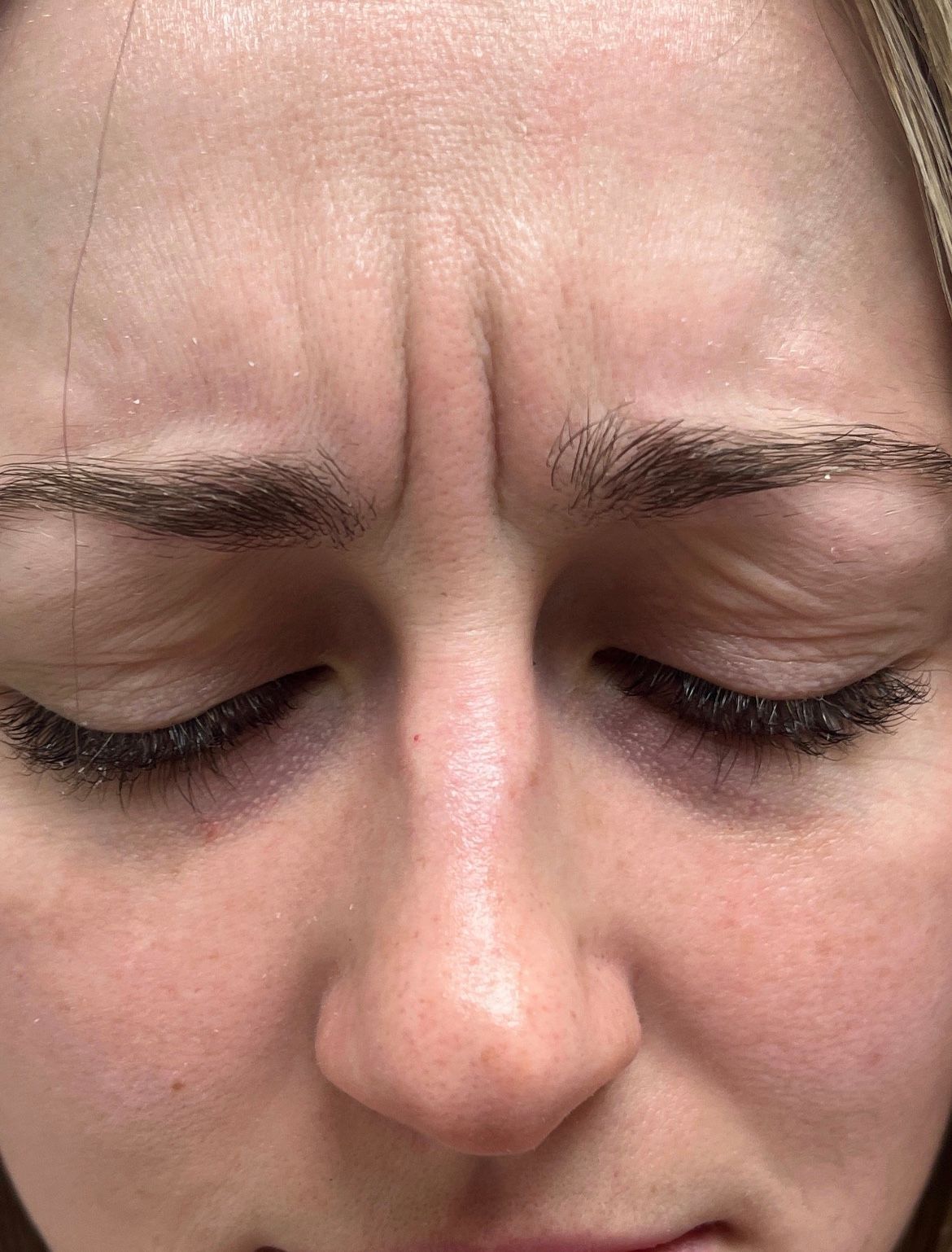 A woman with closed eyes, prominent frown lines between her eyebrows.