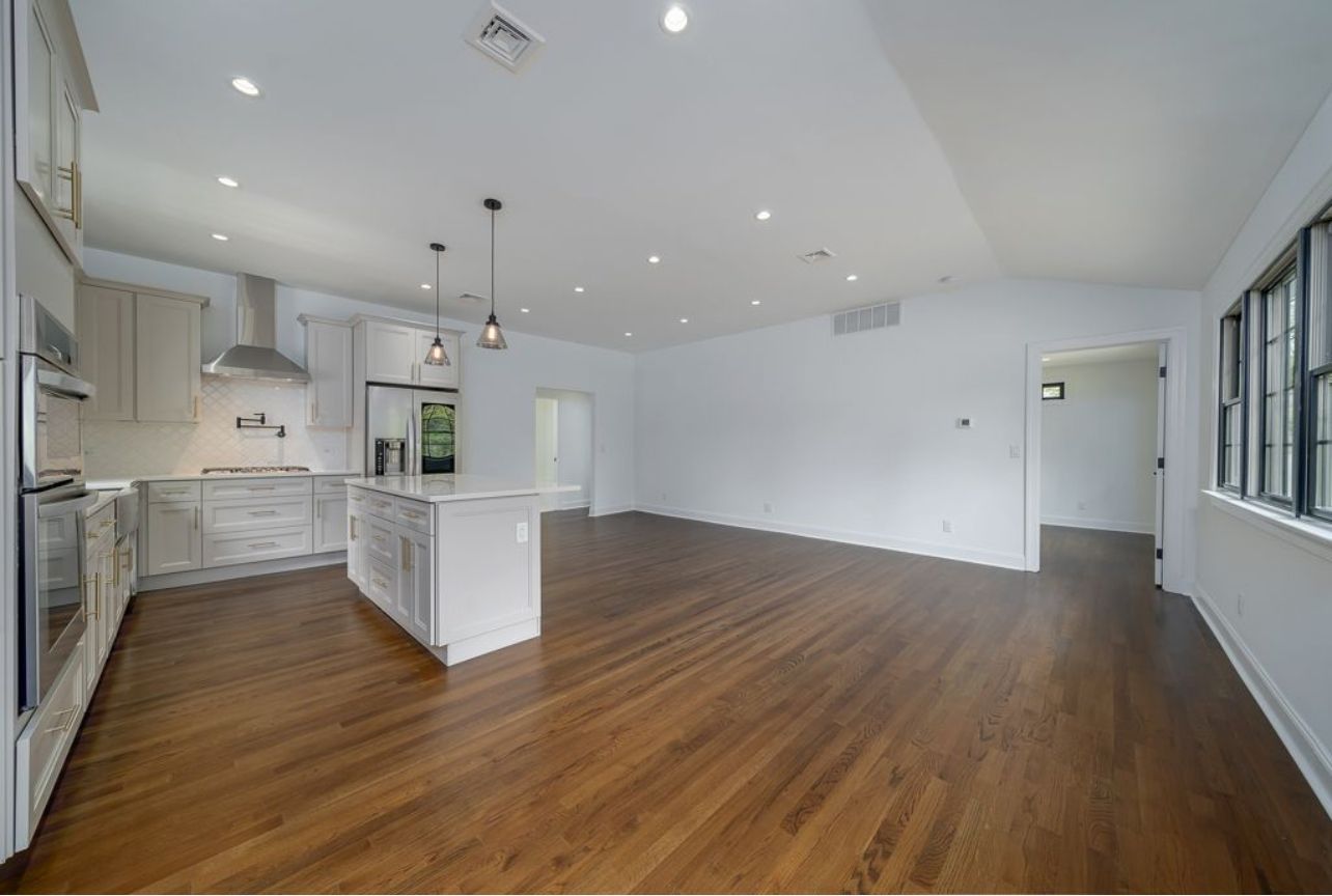 An empty kitchen with hardwood floors and white cabinets.