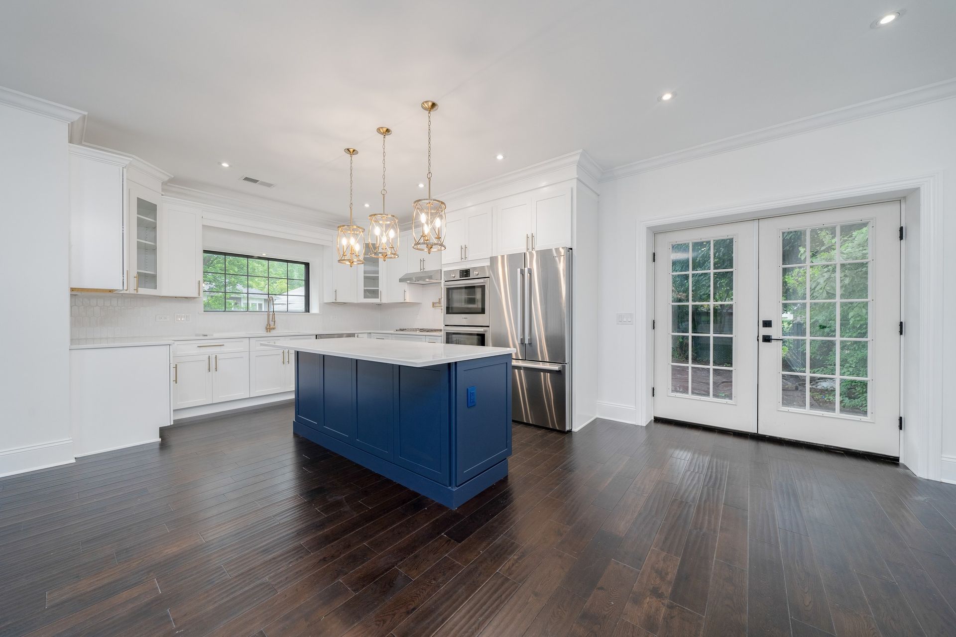 A kitchen with a blue island , white cabinets , stainless steel appliances and hardwood floors.