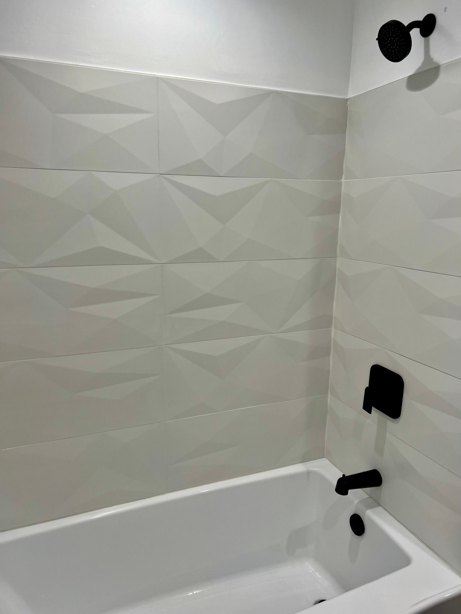 A bathtub in a bathroom with white tiles and a black shower head.