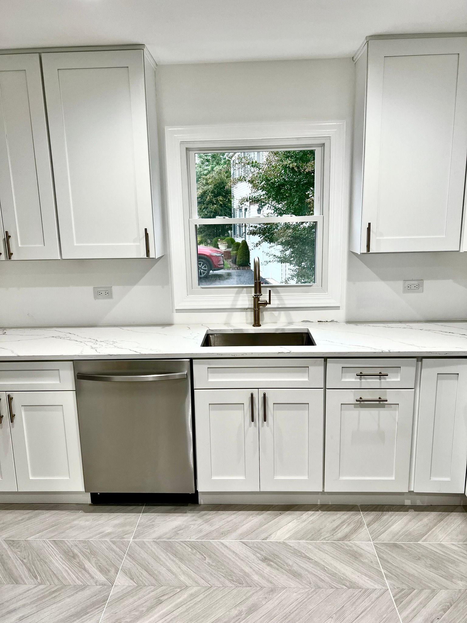 A kitchen with white cabinets , stainless steel appliances , a sink and a window.