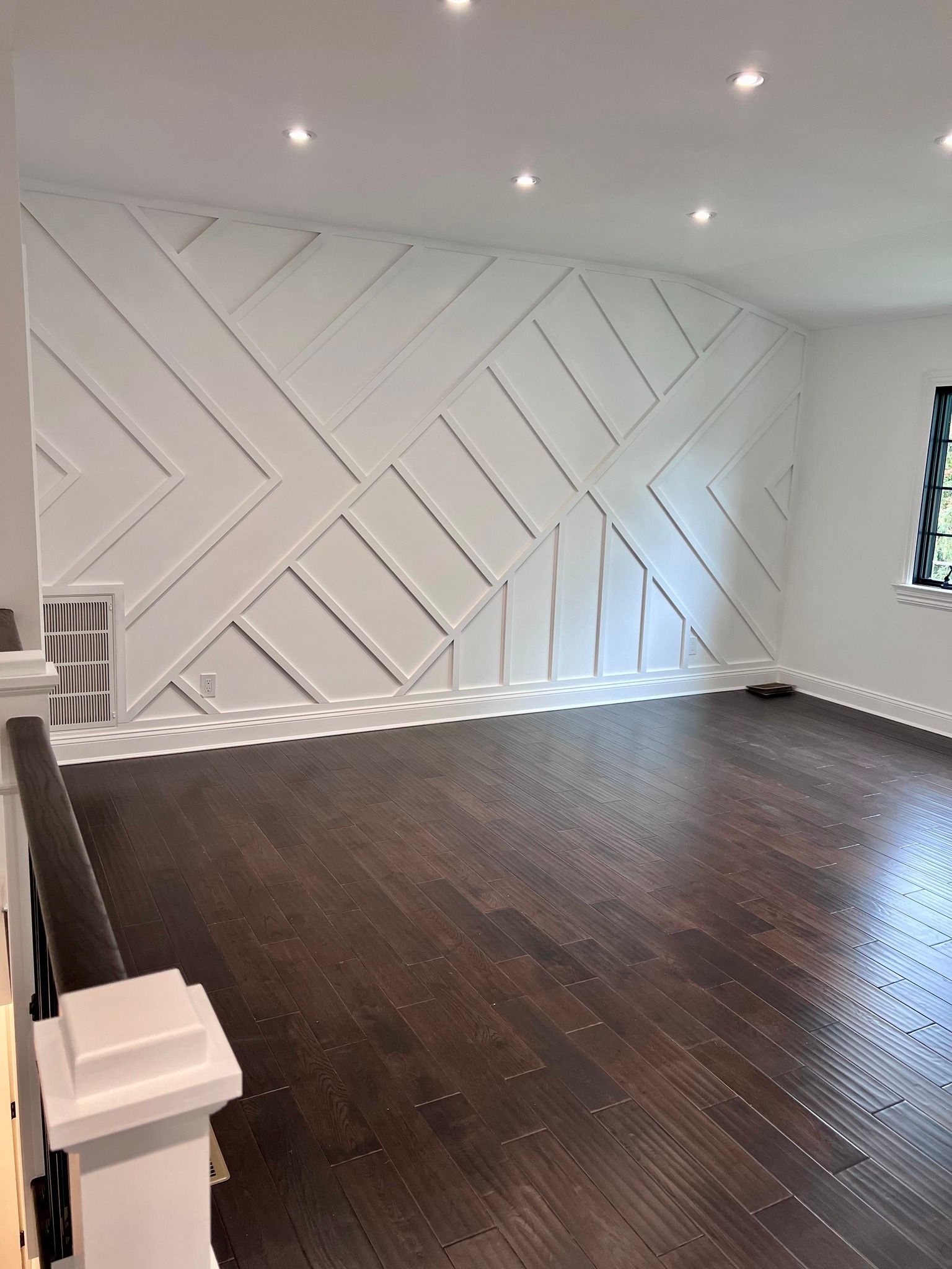 A large empty room with a wooden floor and a white wall.
