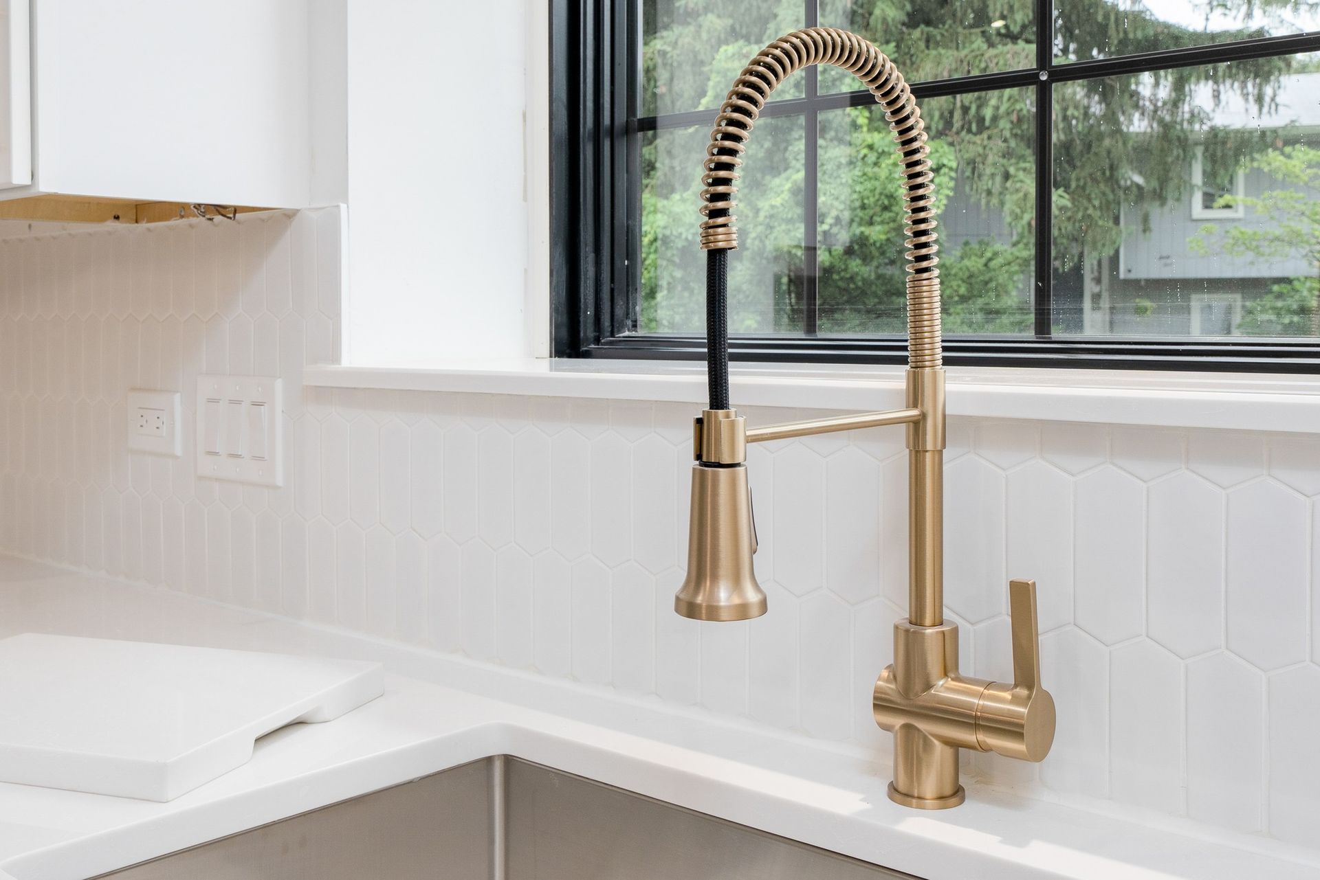 A kitchen sink with a gold faucet and a window.