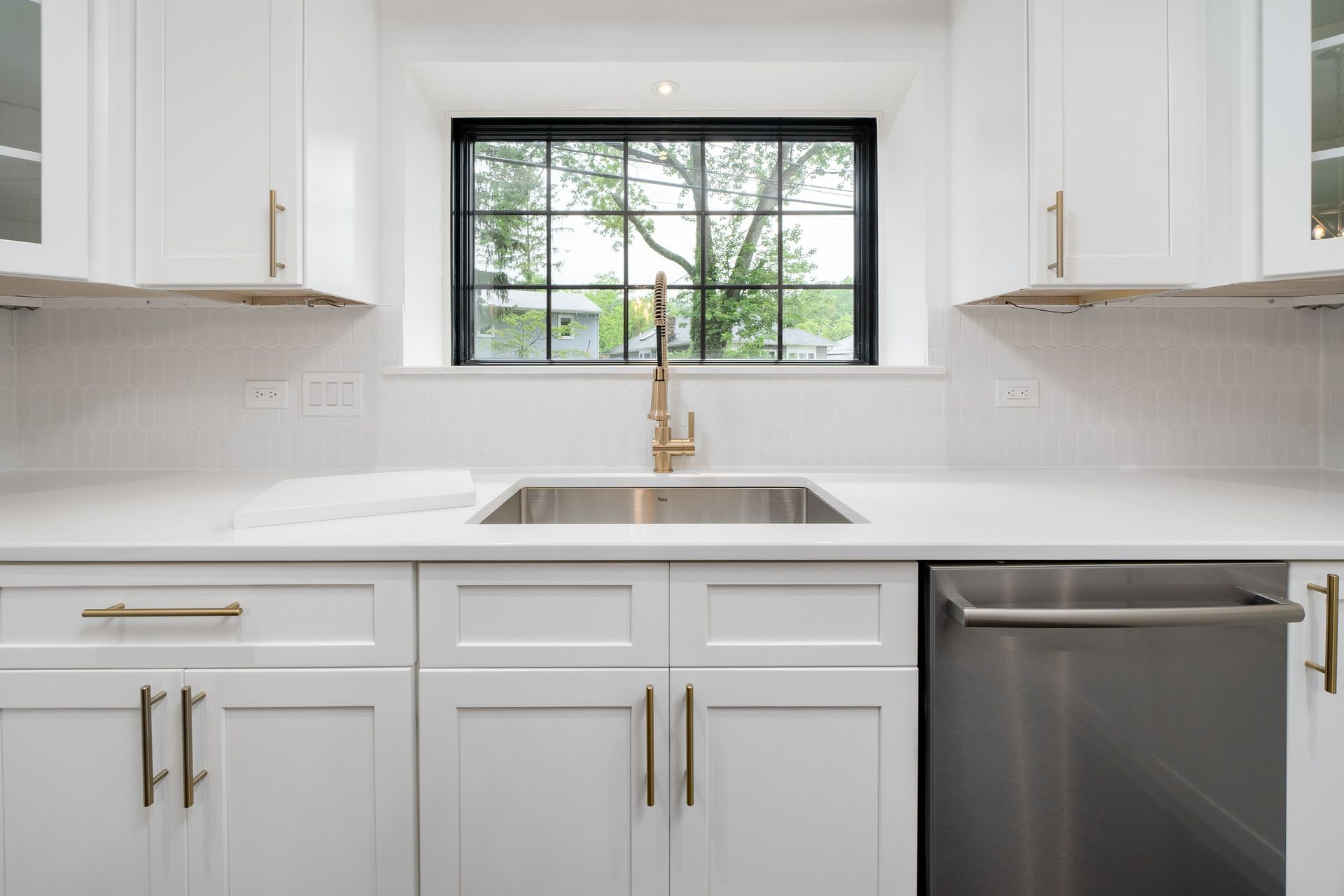 A kitchen with white cabinets , stainless steel appliances , a sink and a window.