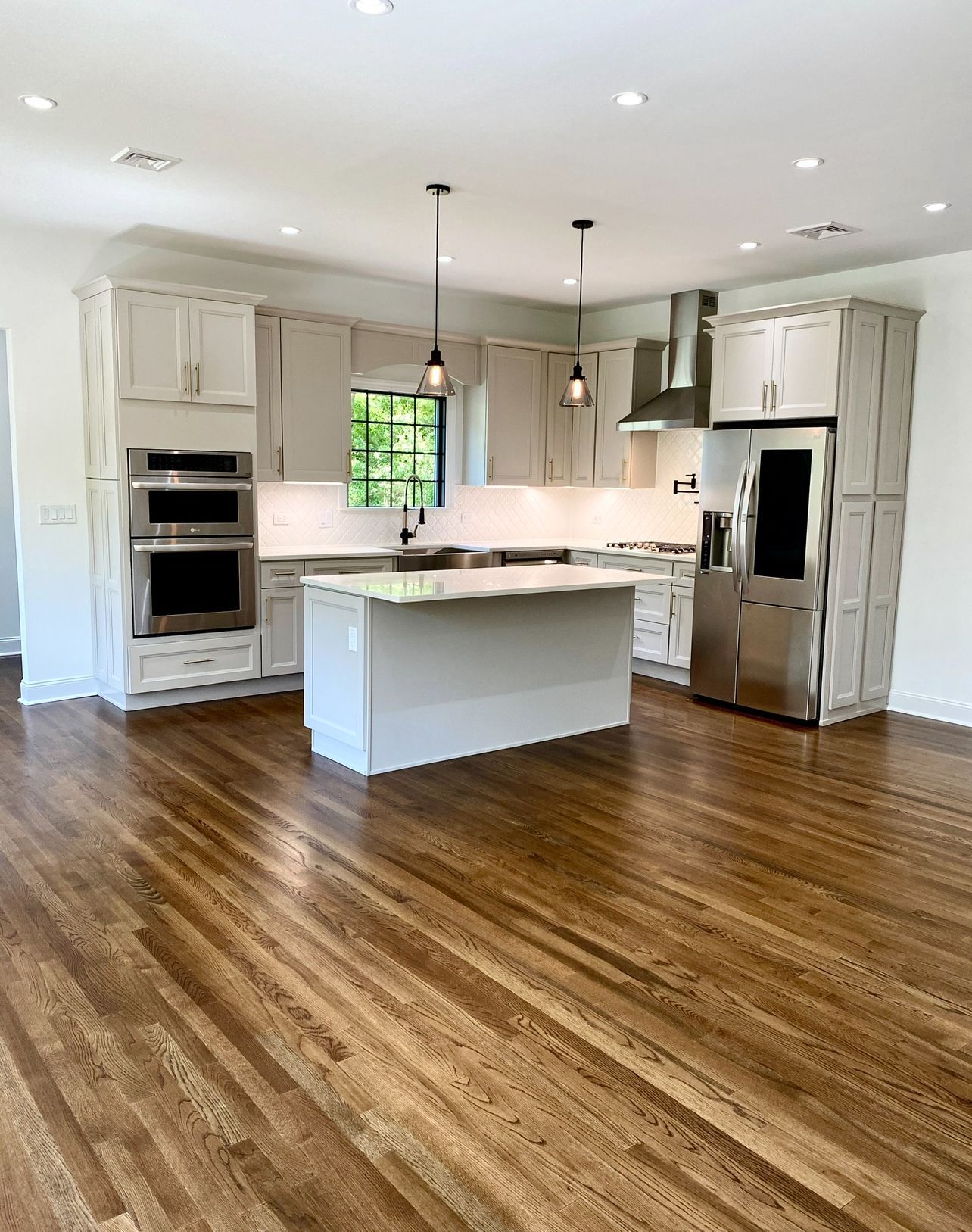 A kitchen with hardwood floors and white cabinets and stainless steel appliances.