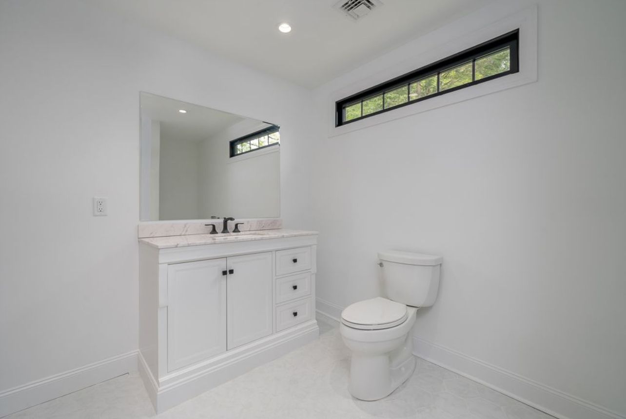 A bathroom with a toilet , sink , mirror and window.