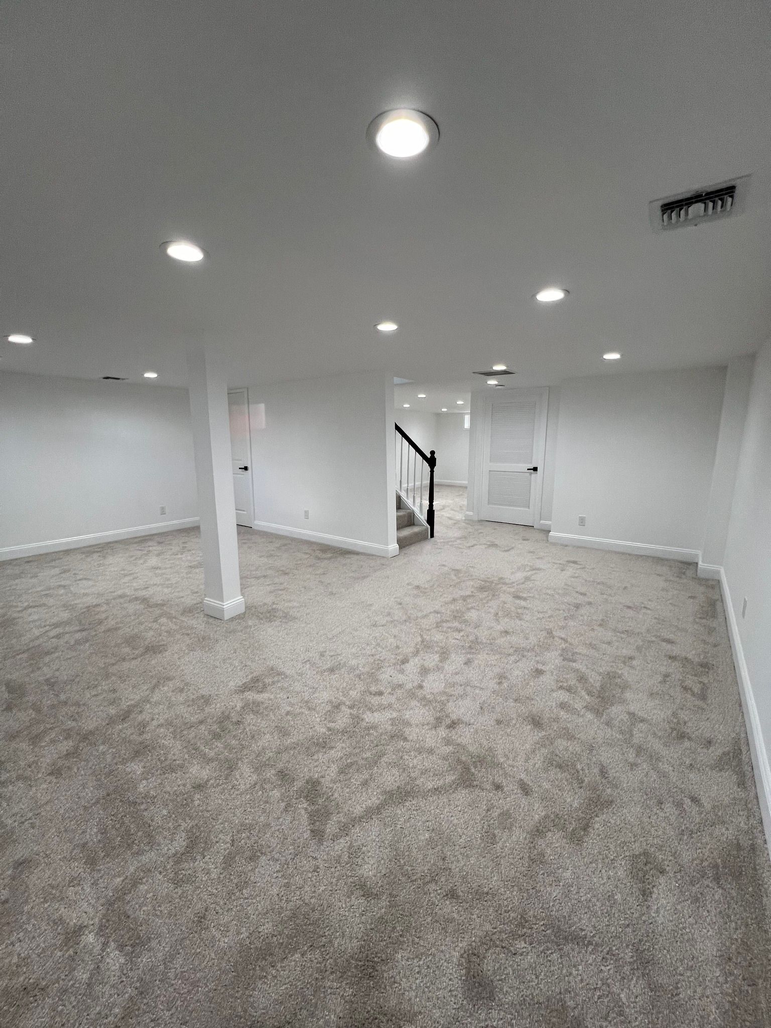 An empty basement with carpeted floors and white walls.
