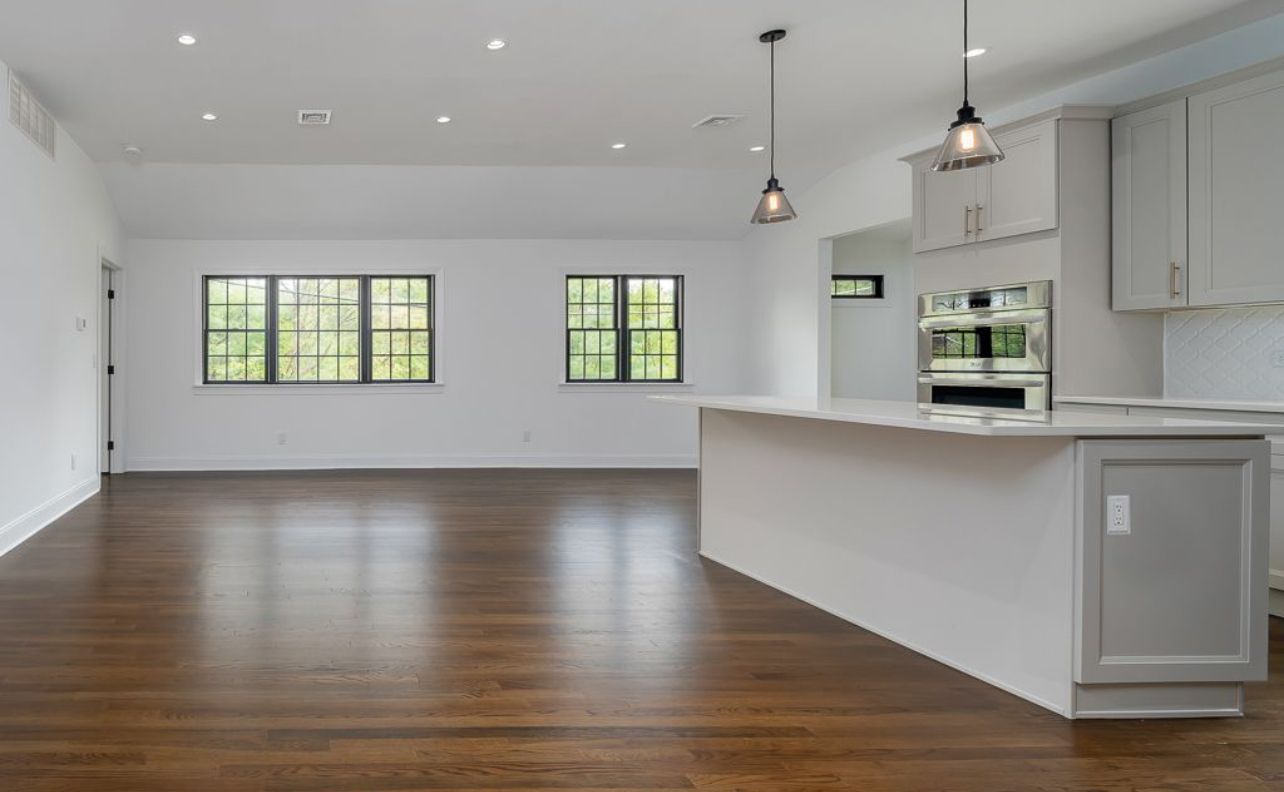 An empty kitchen with hardwood floors and white cabinets.