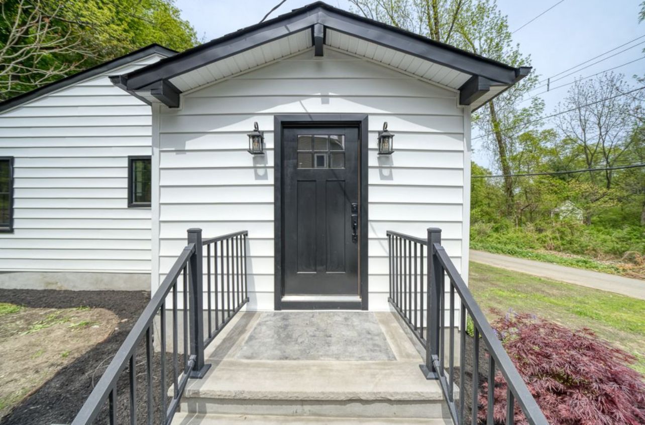A white house with a black door and stairs leading to it.