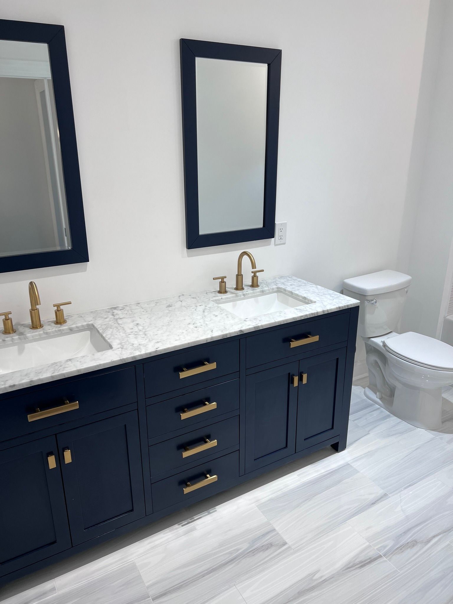 A bathroom with two sinks , two mirrors and a toilet.