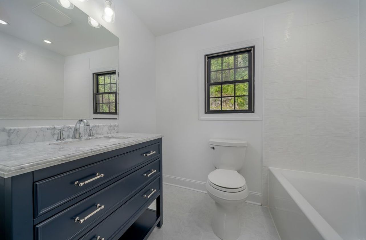 A bathroom with a toilet , sink , mirror and tub.