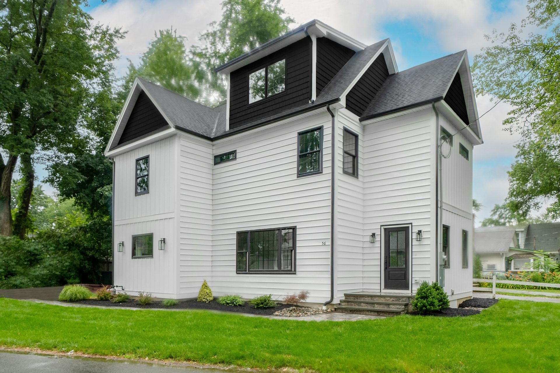A large white house with a black roof is sitting on top of a lush green lawn.