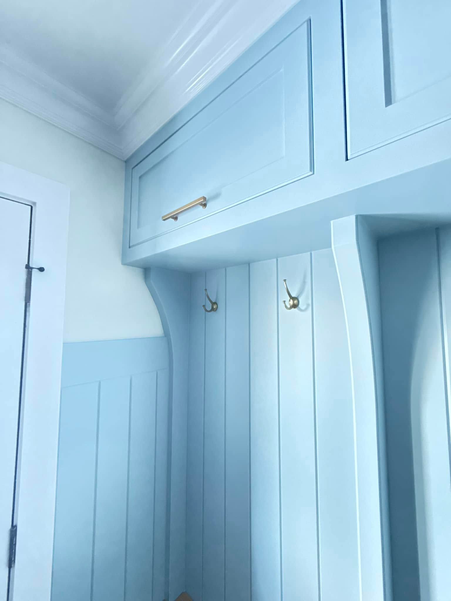 A hallway with blue cabinets and hooks on the wall.