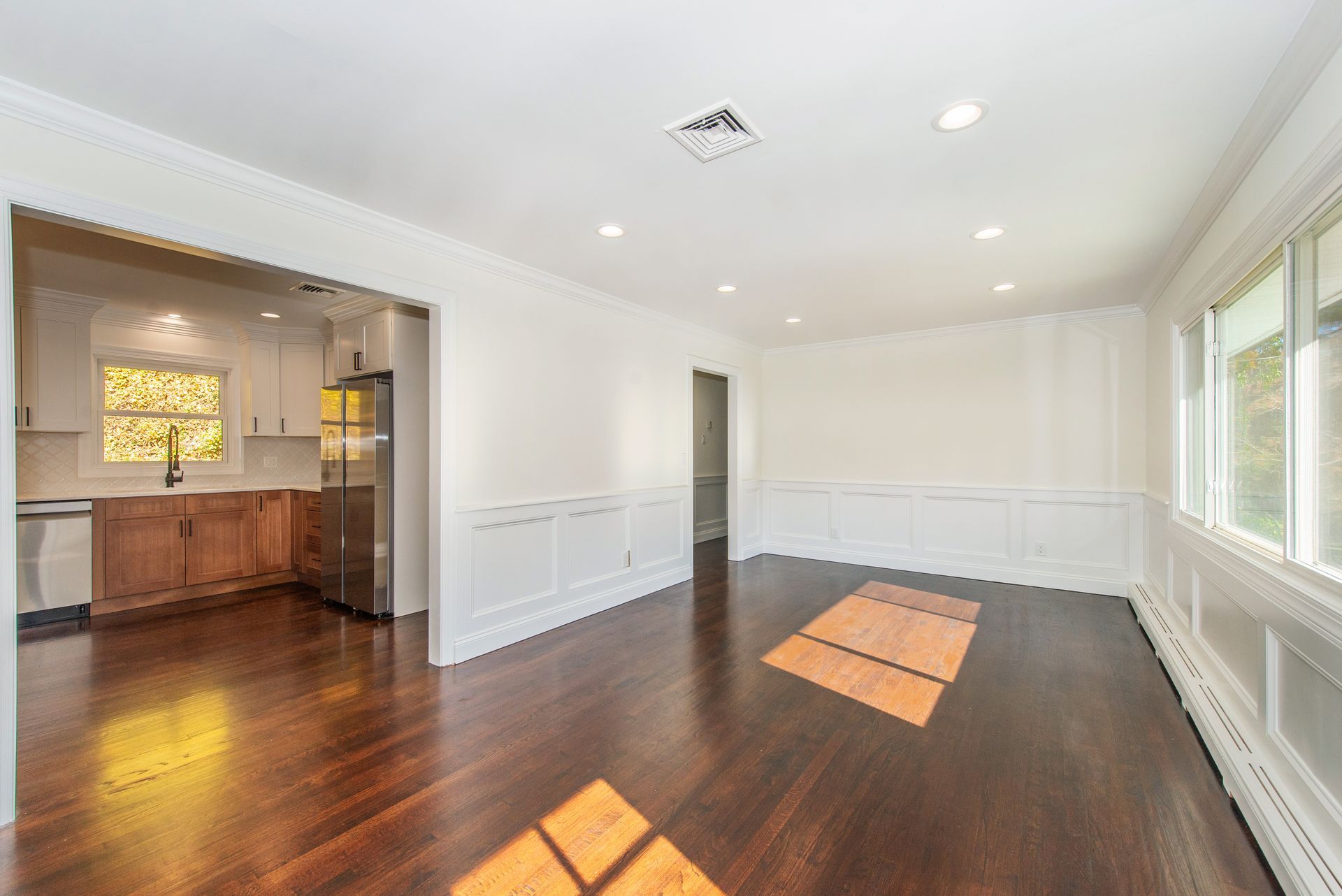 An empty living room with hardwood floors and a kitchen in the background.