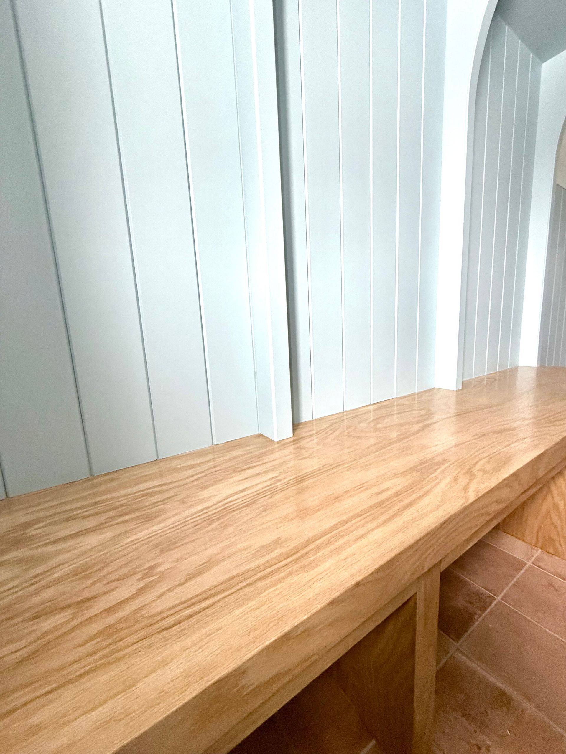 A wooden bench is sitting in front of a white wall.