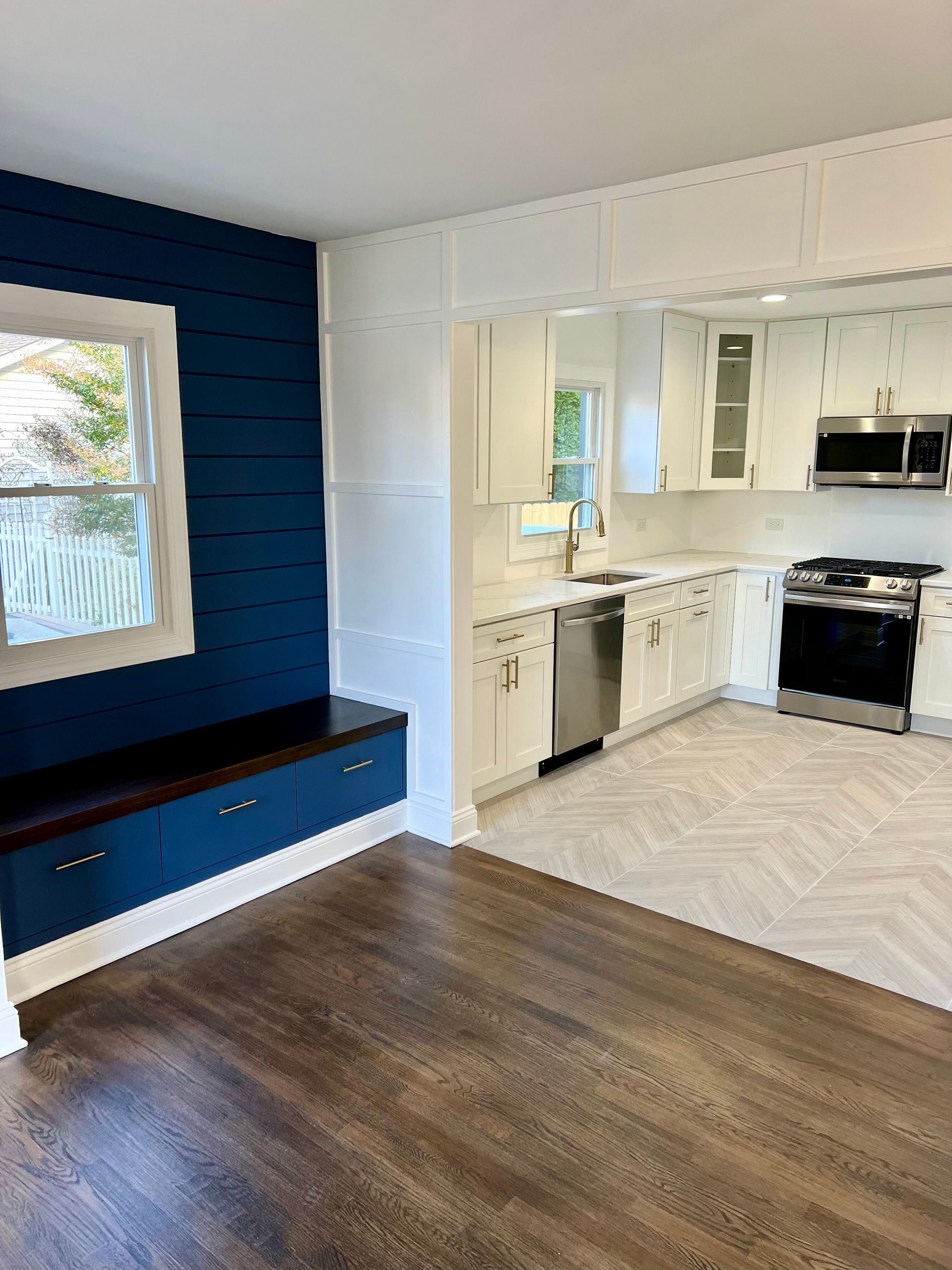A kitchen with blue walls , white cabinets , stainless steel appliances and hardwood floors.
