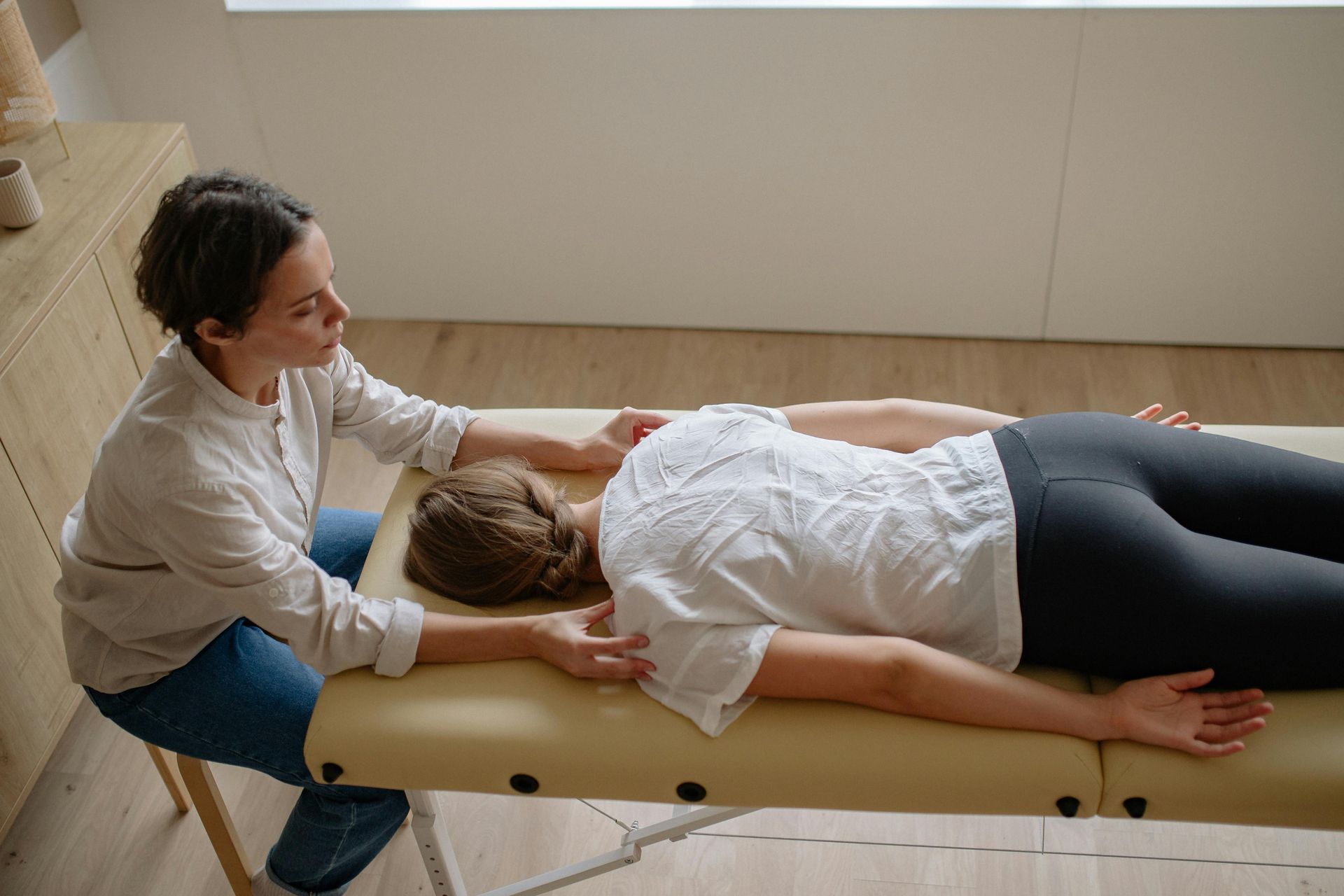 Therapist performing a back massage on a woman lying face down on a treatment table.