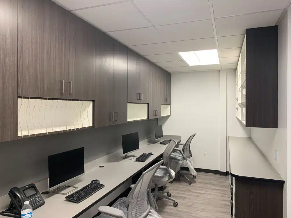 A row of desks with computers and chairs in an office.