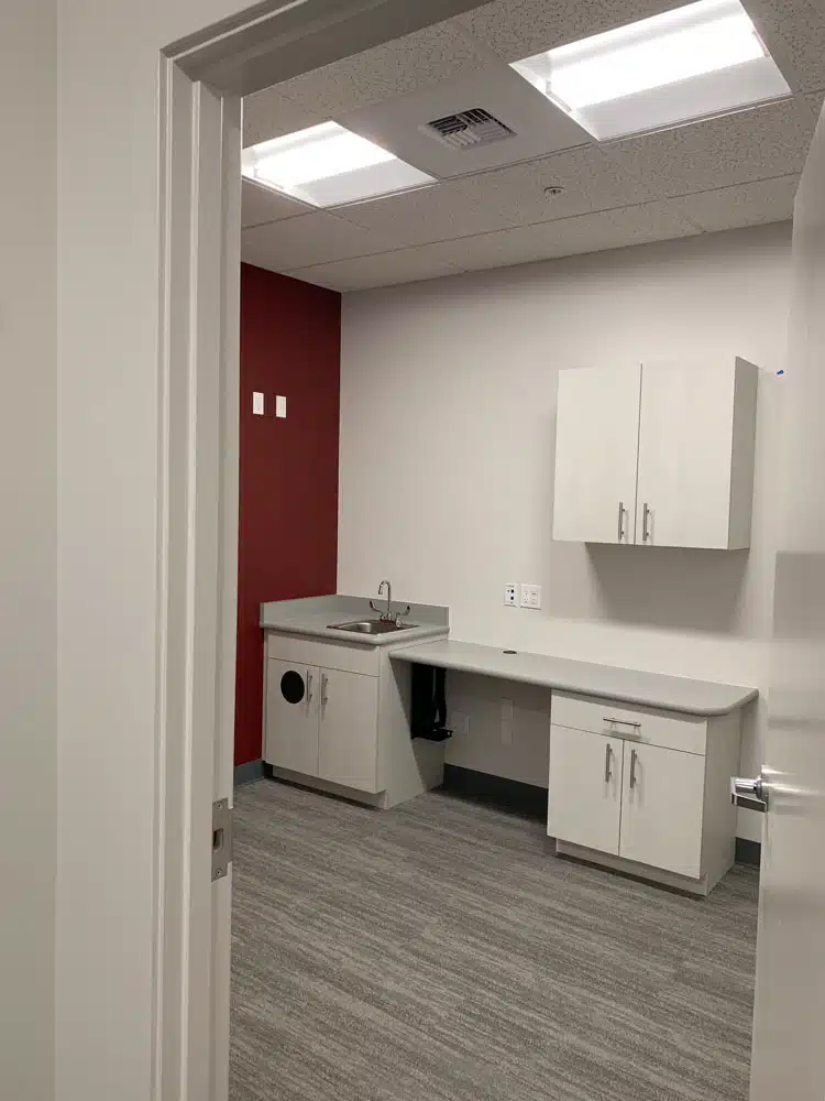 A room with a sink , cabinets , and a red wall.