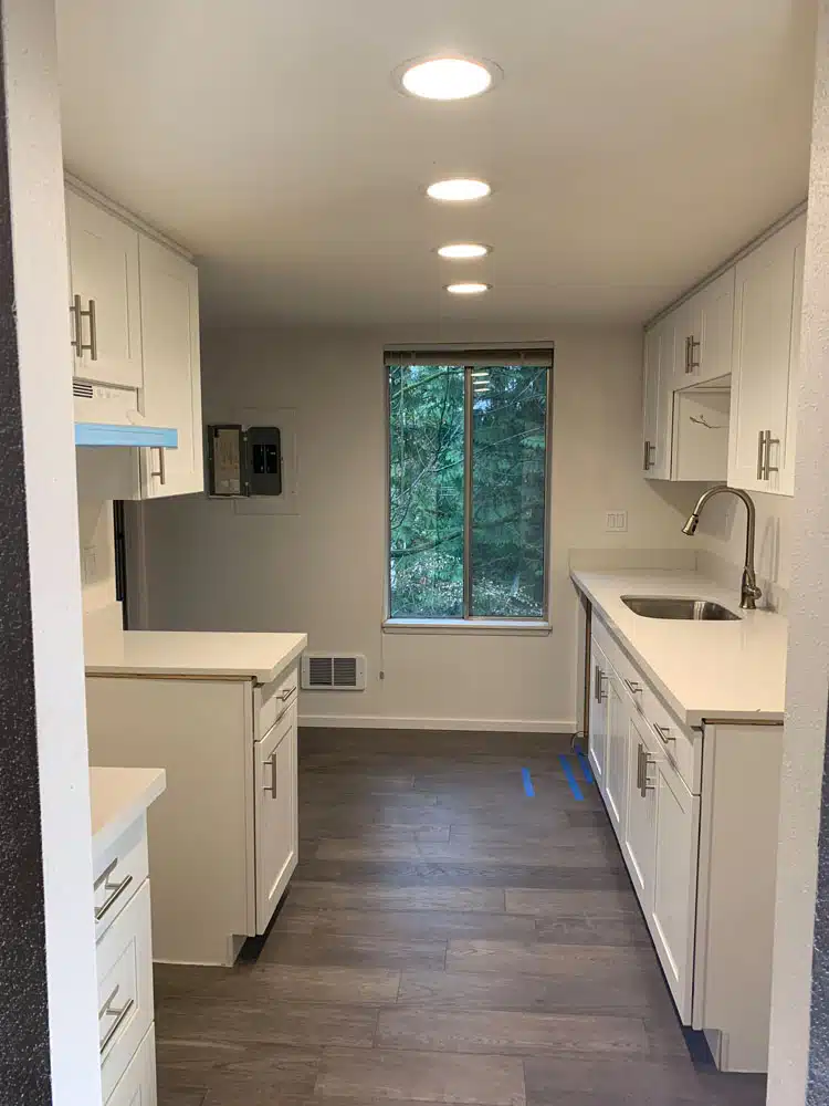 A kitchen with white cabinets , a sink , and a window.