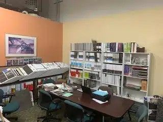 A conference room with a table , chairs , shelves and a laptop.