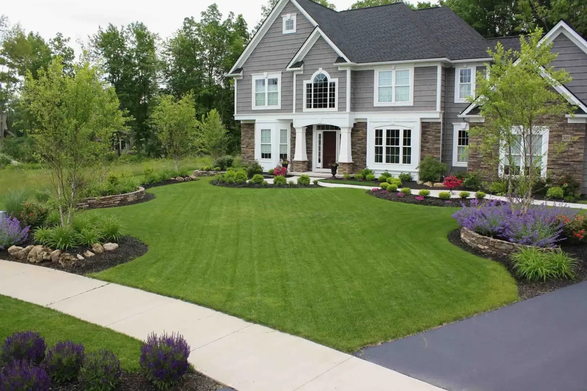 A large house with a lush green lawn and purple flowers