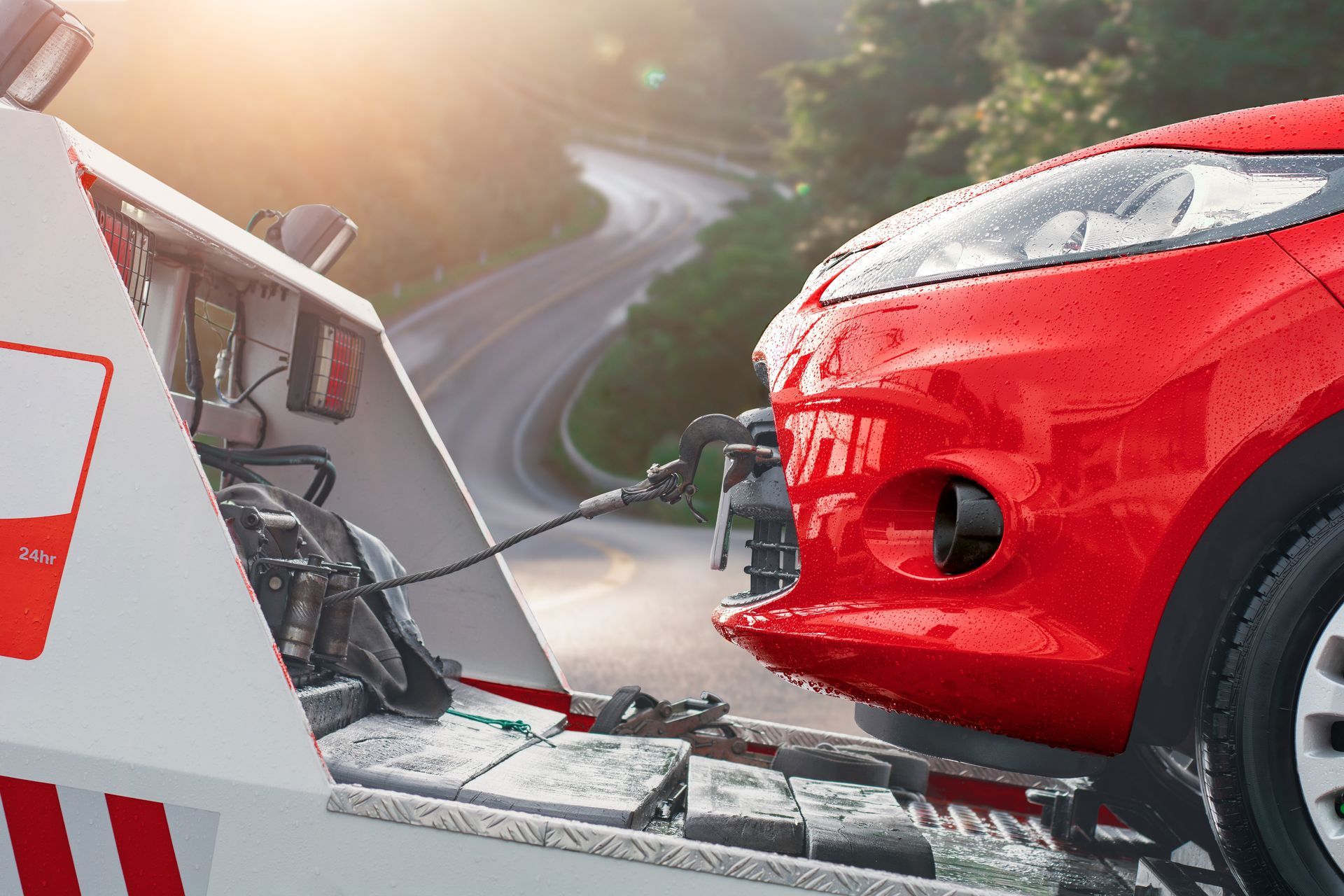 Red car being loaded onto a tow truck on a winding road at sunset