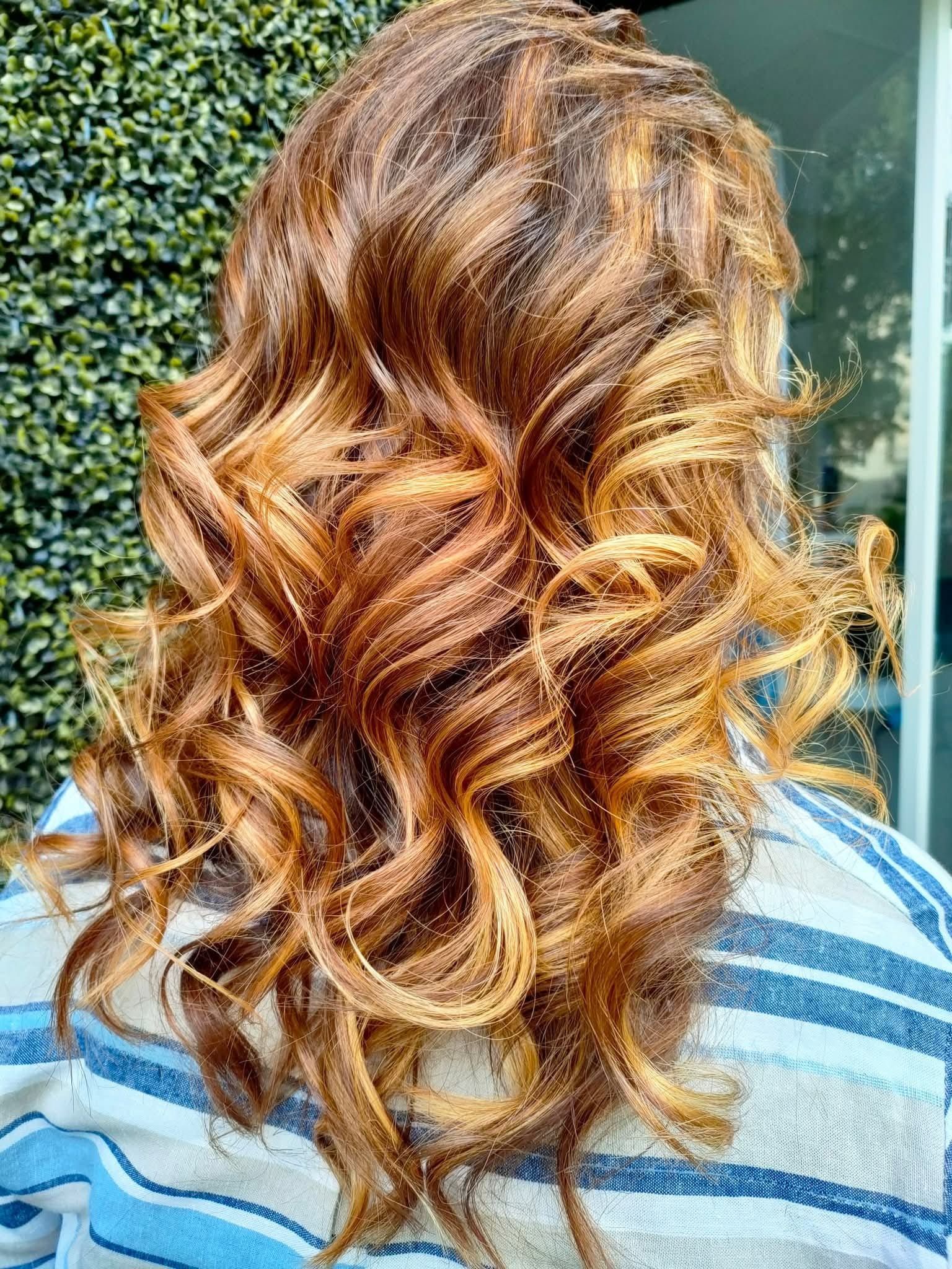 Vista posteriore di lunghi capelli ondulati con riflessi castano dorato e radici scure, acconciati in morbidi ricci.