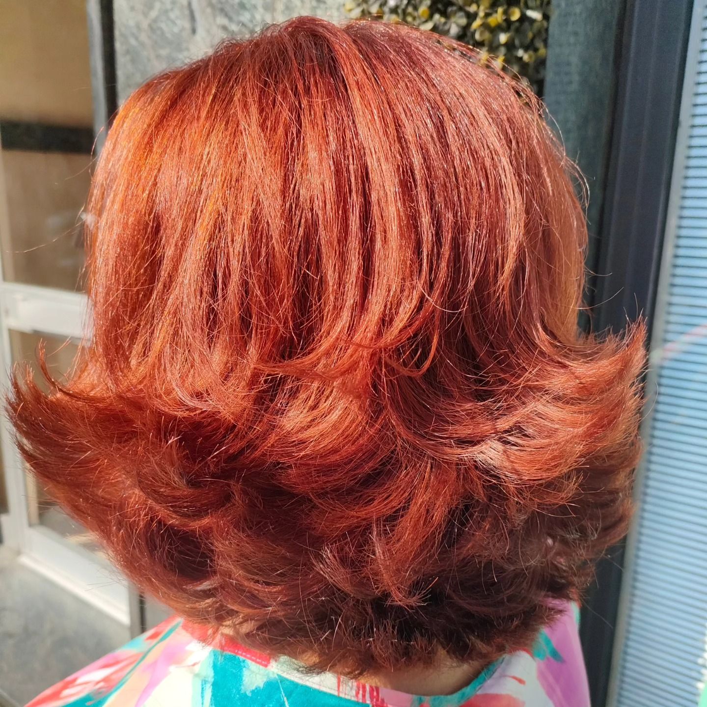 La parte posteriore della testa di una persona che mostra capelli di media lunghezza, scalati, di un vibrante rosso rame, acconciati con le punte rivolte verso l'esterno.