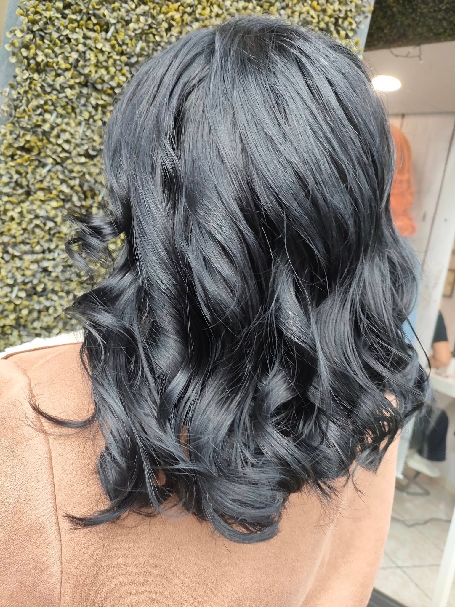 Vista posteriore di una persona con capelli scuri e ondulati, acconciati in trecce sottili e fitte che si trasformano in morbidi ricci alle punte.