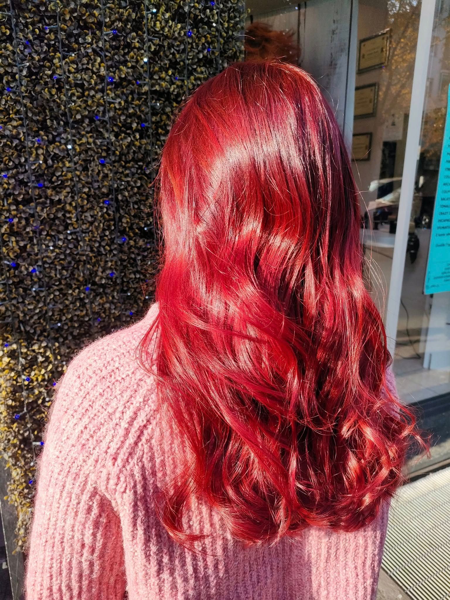 Una persona con lunghi capelli rosso vivo e onde morbide, che indossa un maglione rosa a trama, in piedi all'aperto.