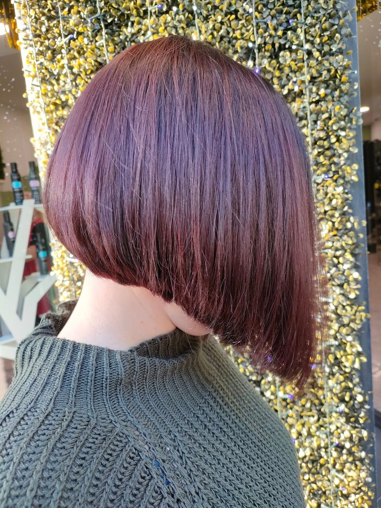 Una vista di profilo di un elegante caschetto asimmetrico color castano rossiccio scuro, su uno sfondo di fili dorati.