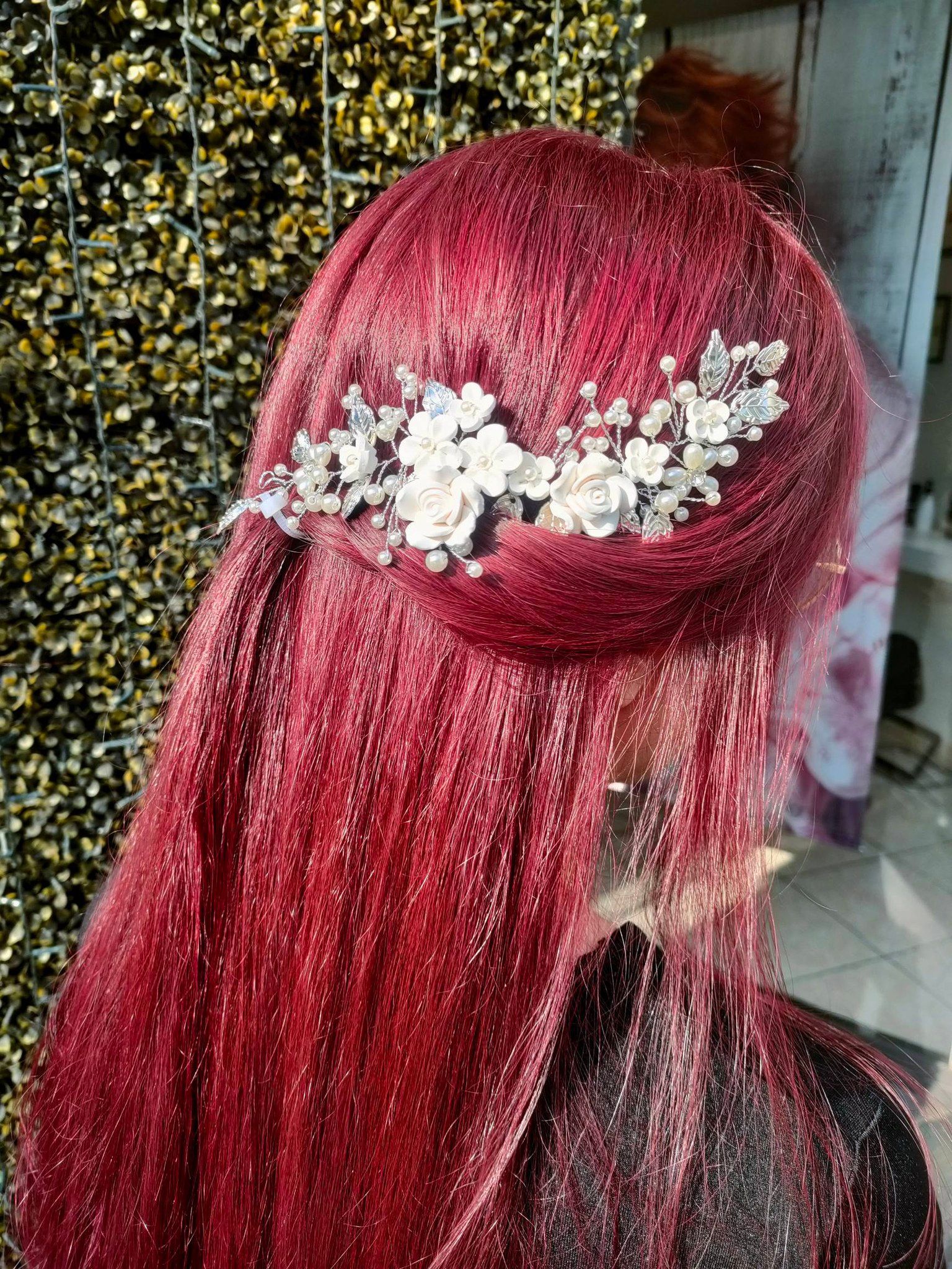 Vista posteriore di capelli rosso vivo e dalla texture particolare, raccolti a metà con un delicato accessorio floreale argentato.