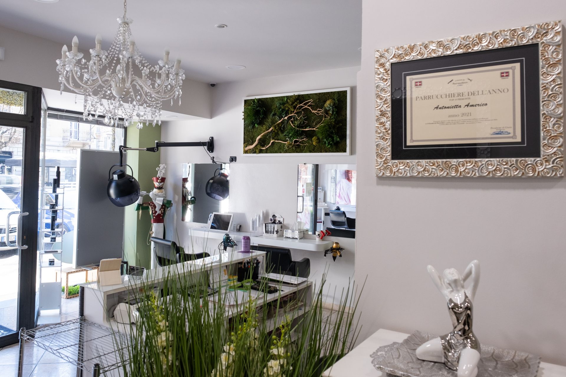 Un salone da parrucchiere moderno e luminoso, con un lampadario di cristallo, specchi, asciugacapelli e quadri alle pareti.