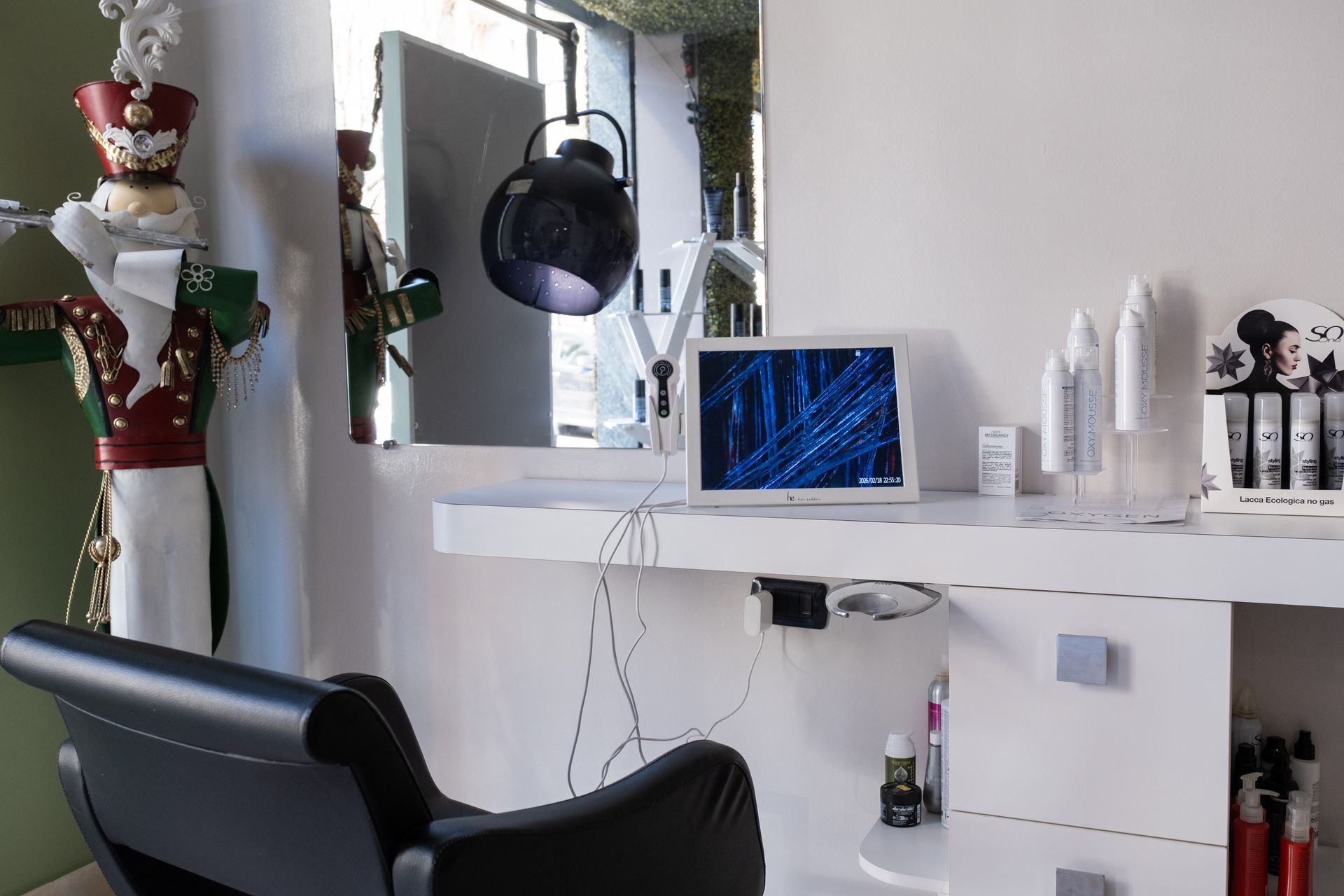 Una postazione da parrucchiere con una sedia nera, uno specchio illuminato, un ornamento a forma di schiaccianoci e scaffali pieni di prodotti per capelli.